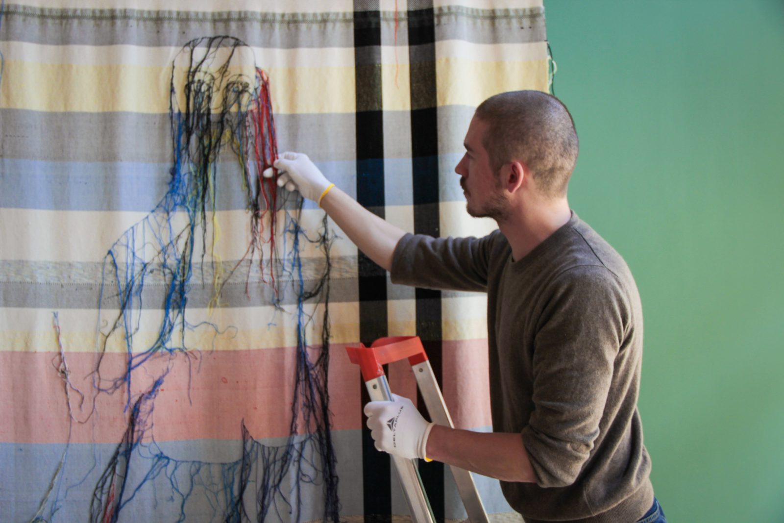 The technician of Institut finlandais Quentin L’hôte installing a tapestry by Sonja Jokiniemi.